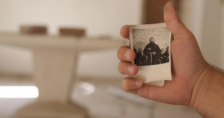 قس في كنيسة الروم الأرثوكس بجسر الشغور يحمل صورة لأتباع الكنيسة الذين غادر معظمهم خلال الحرب السورية، تموز 2020، المصدر: (عنب بلدي)