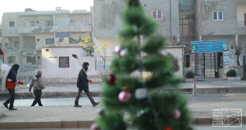 صورة خاصة بسوريون من أجل الحقيقة والعدالة تُظهر سكاناً محلّيين من مدينة الرقة يمشون أمام متجر لبيع أشجار أعياد الميلاد.